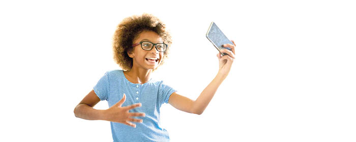 A smiling child holding up a phone to record her dancing