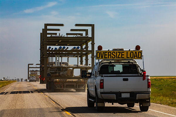 a car with a sign that reads "oversize load" following behind a truck