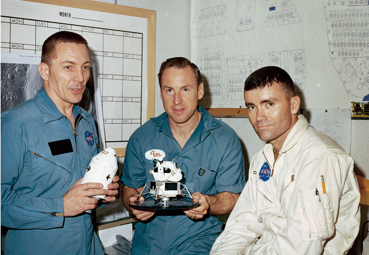 Three men in NASA uniforms holding spacecraft models