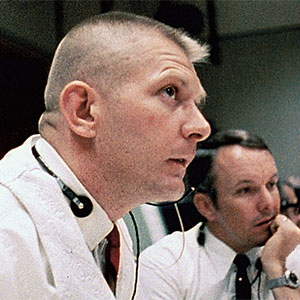 Man in a white shirt and red tie looks upward as a man dressed the same way sits beside him
