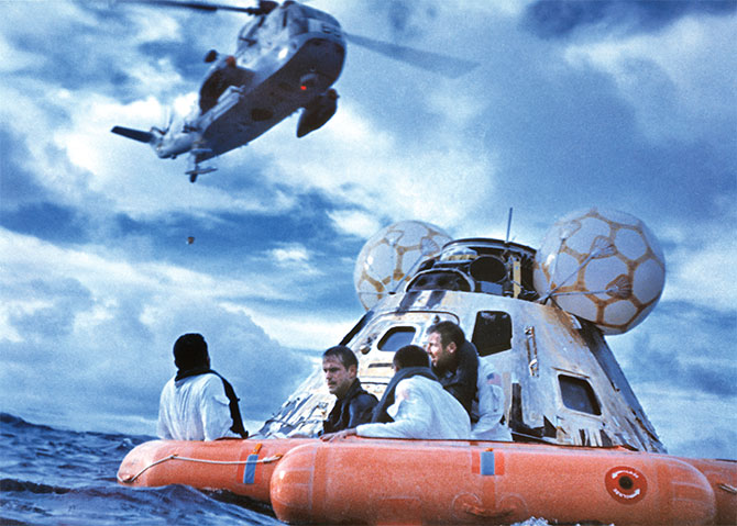 Enlargeable photo of four astronauts in a floating raft as a helicopter flies overhead