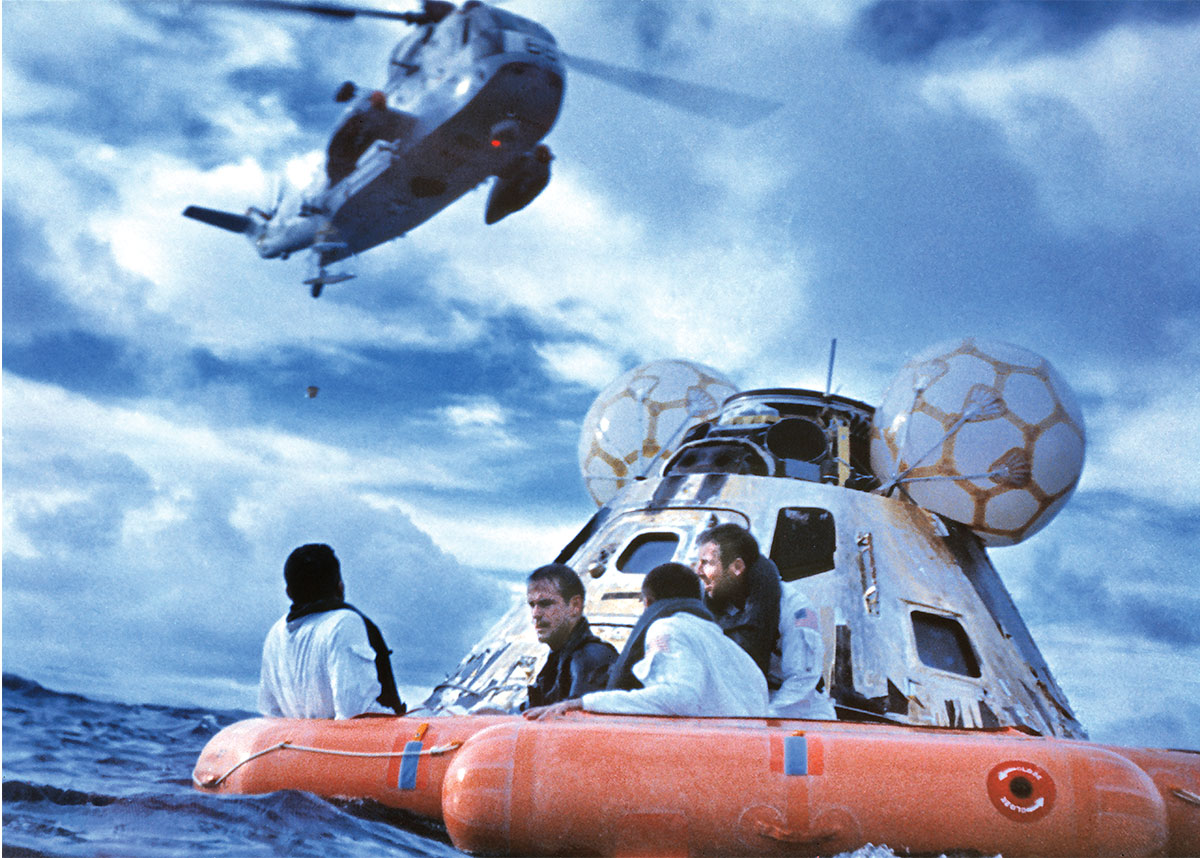 Four astronauts in a floating raft as a helicopter flies overhead